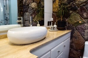 A bathroom with a large white sink, a stone wall, and a mirror.