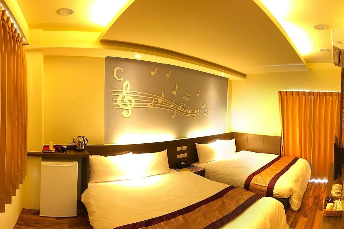 Quarto de hotel com duas camas, uma pequena escrivaninha e um painel decorado com notas musicais.