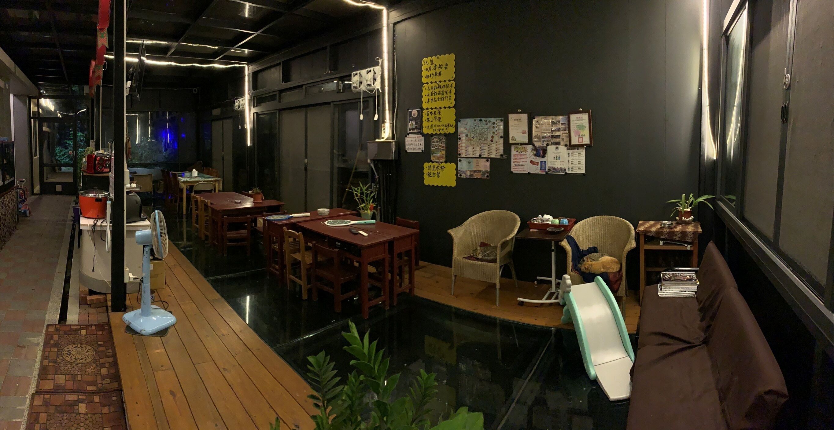 A cozy restaurant with wooden tables and chairs, a fan, and a small sofa.