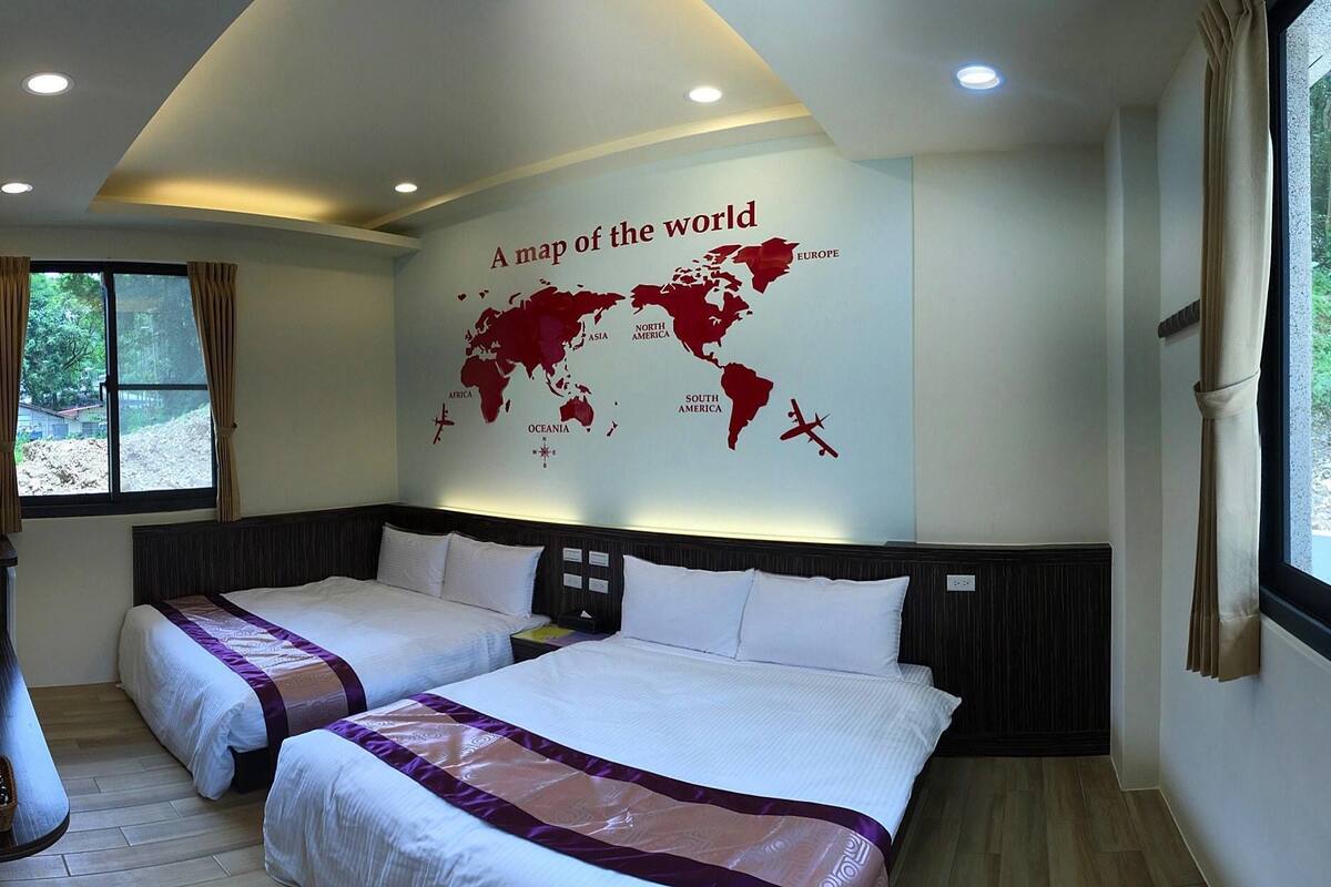 Quarto de hotel com duas camas, um mapa-múndi na parede e uma janela com cortinas.
