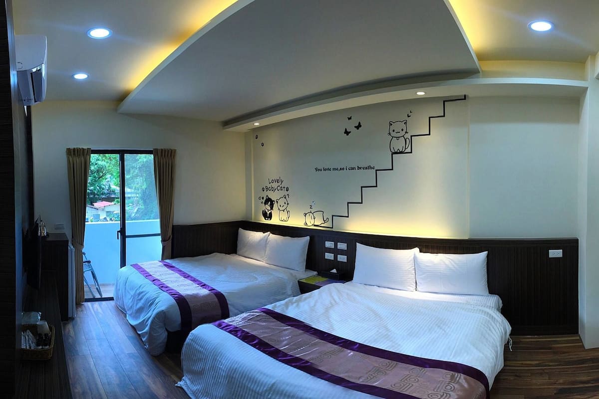 Quarto de hotel com duas camas, arte na parede da escada e vista para o verde lá fora.