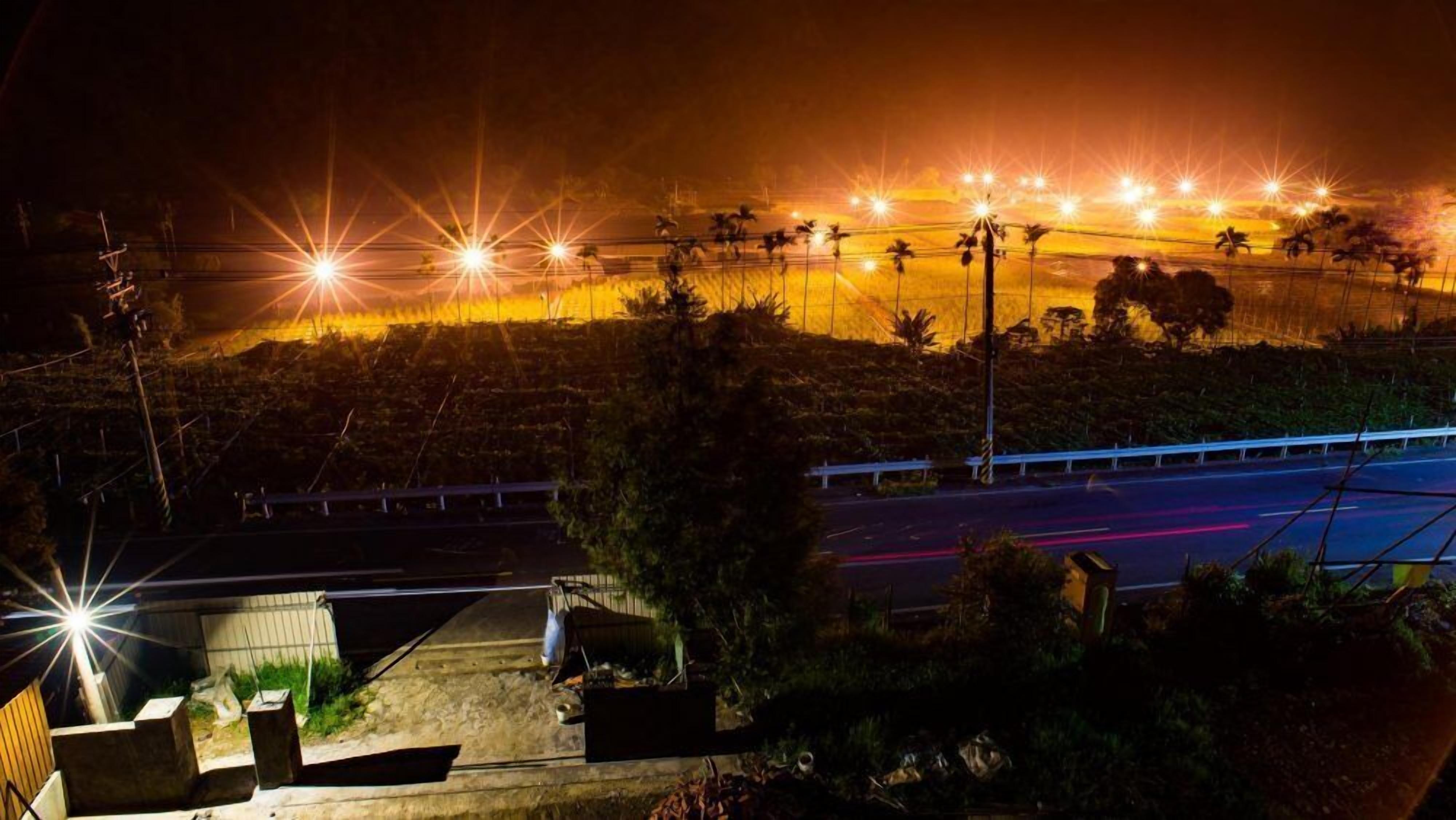 A nighttime view of a road with streetlights and a guardrail.