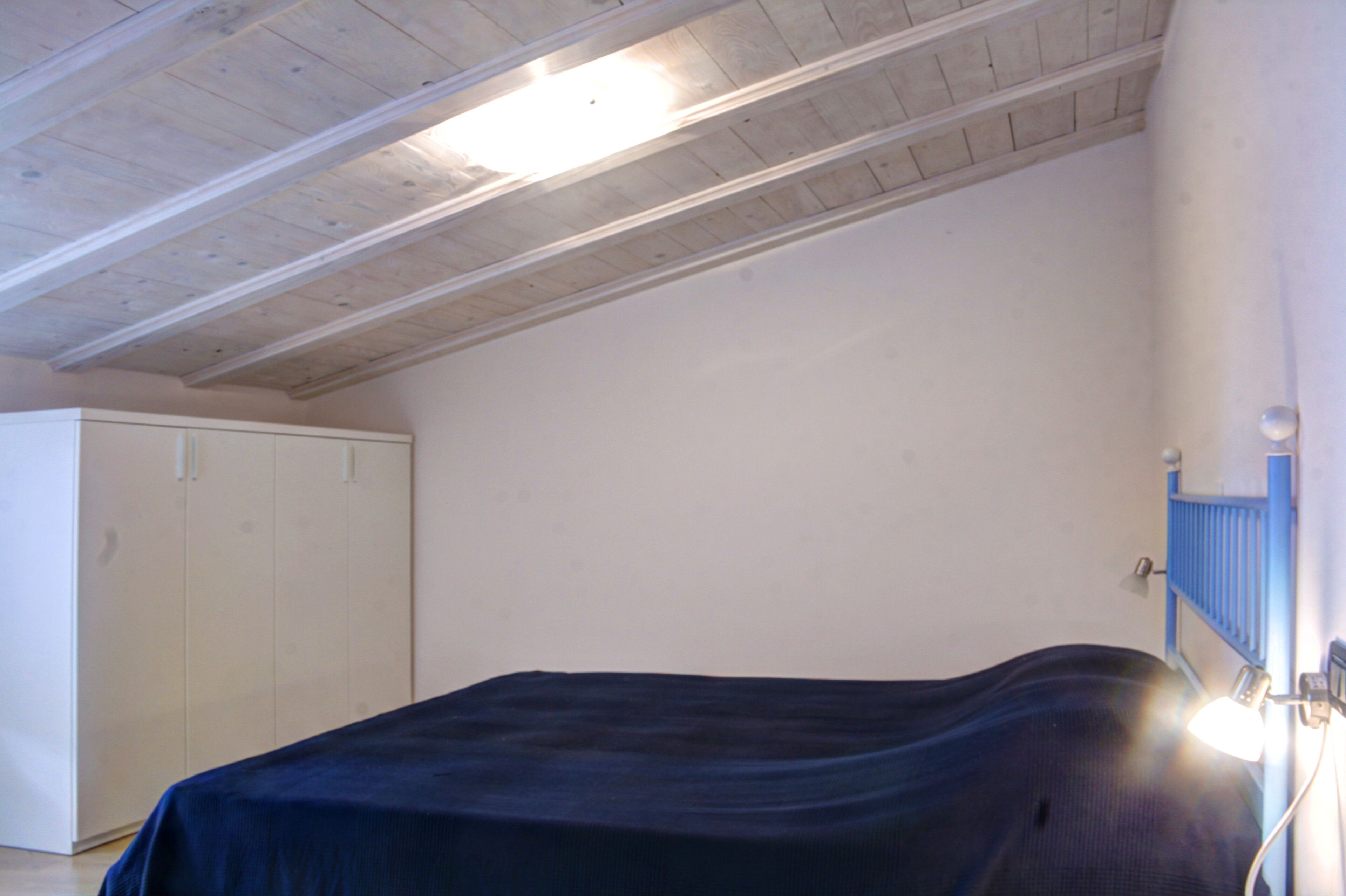 Une chambre à coucher comprenant un lit, une armoire et un plafond avec des poutres apparentes.