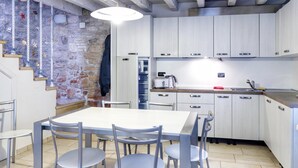 Una cocina moderna con armarios blancos, una mesa de comedor con sillas y una pared de piedra con detalles decorativos.