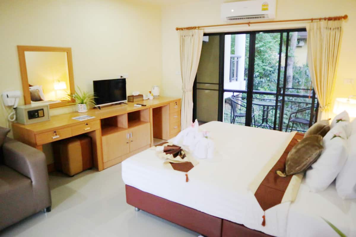 A hotel room with a bed, a desk with a television, a mirror, and a window with curtains.