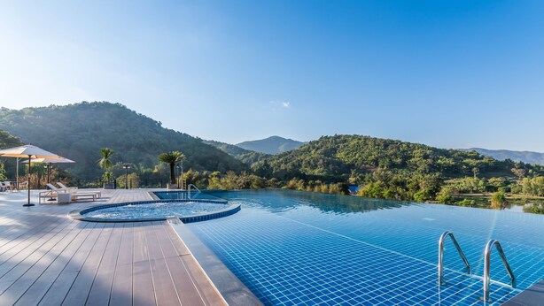 Una piscina con cubierta de madera y sillas de descanso, rodeada de abundante vegetación y colinas.