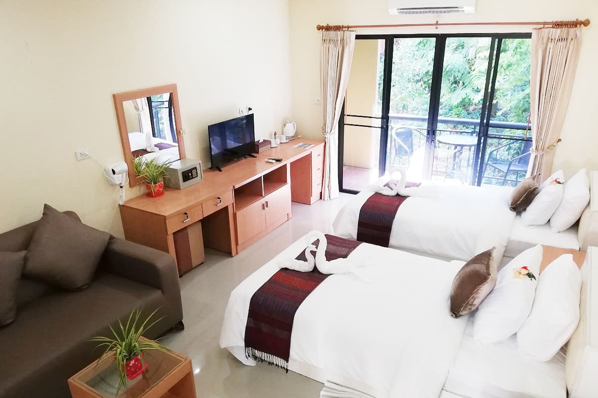 A hotel room with two beds, a sofa, a desk with a TV, a mirror, and a window with curtains.