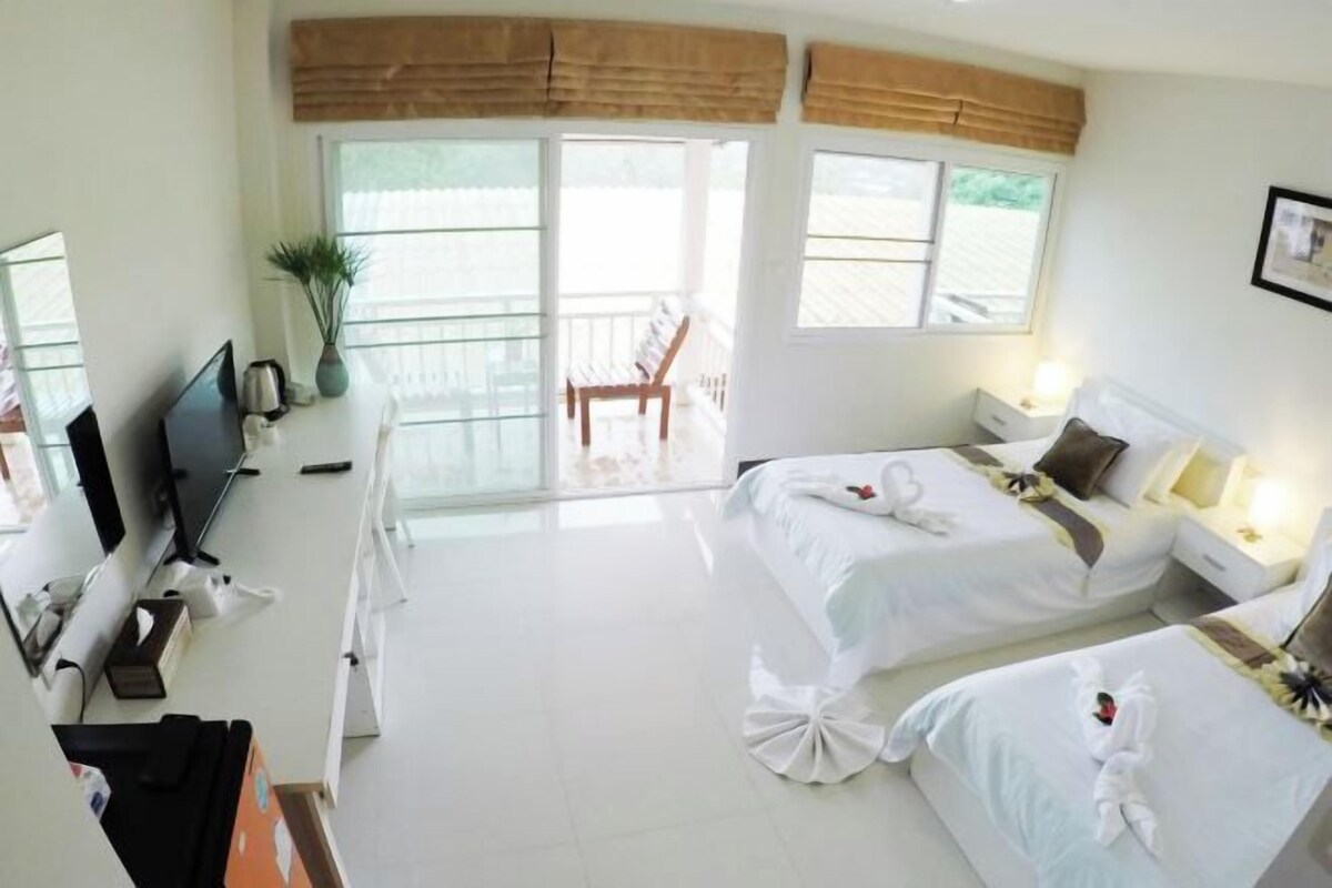 A hotel room with two beds, a desk with a computer, a chair, and a balcony with a chair.