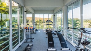 Un gimnasio con equipo de ejercicio, ventanas amplias y vistas a zonas verdes.