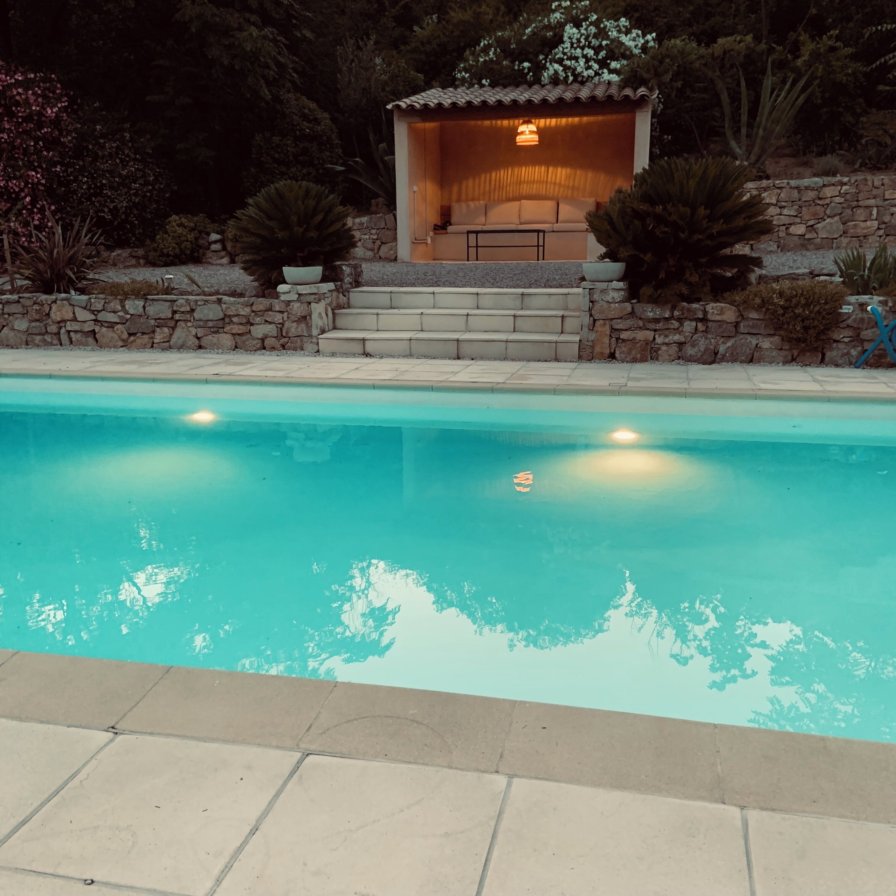 Una piscina amb un mur de pedra i escales que condueixen a una zona d'estar coberta.