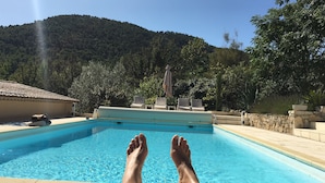 Ein Pool mit klarem, blauem Wasser, umgeben von einer Steinmauer und Blick auf einen bewaldeten Hügel.