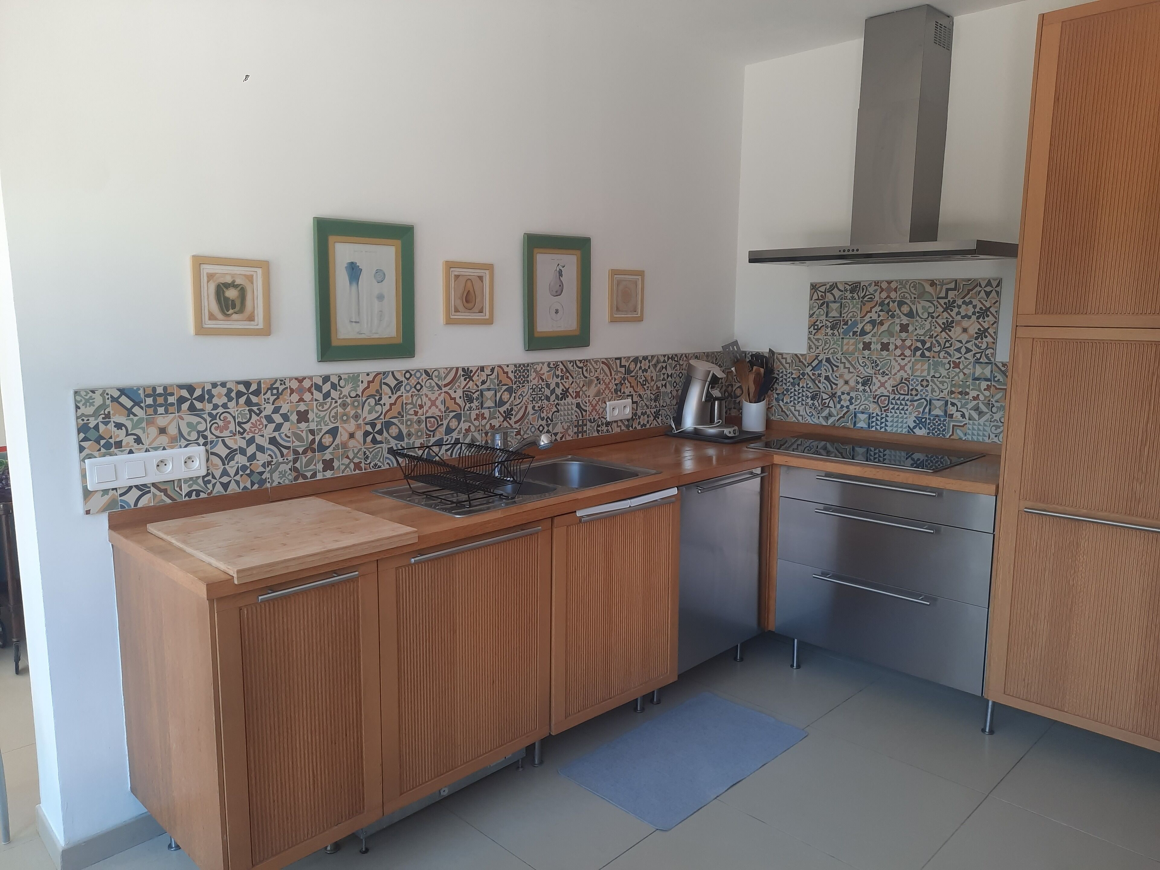 A compact kitchen with wooden cabinets, a tiled backsplash, and a stainless steel sink.