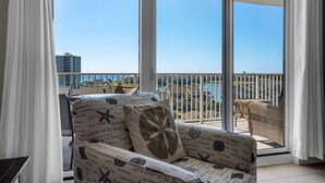 A balcony with a view of the sea and buildings, a wicker chair, and a sofa with a starfish pillow.