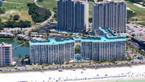 A large hotel complex with multiple high-rise buildings, a beach, and a golf course in the background.
