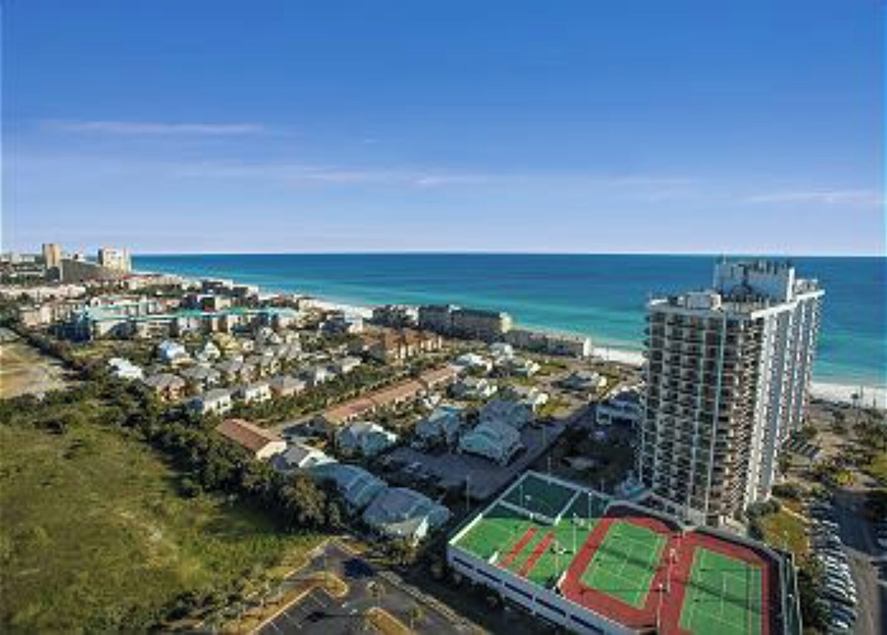 A coastal cityscape with a prominent high-rise hotel, a sports complex, and a beach in the background.
