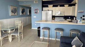 A compact kitchen with white cabinets, a refrigerator, and a microwave. There are two stools and a dining table with chairs. - Read my reviews.  Know what you are getting. (Fort Walton Beach)