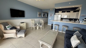 A living room with a sofa, a coffee table, a dining table with chairs, a kitchen area with a fridge, and a ceiling fan. - Read my reviews.  Know what you are getting. (Fort Walton Beach)