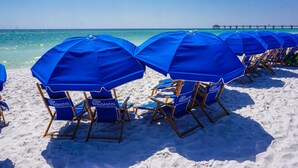A beach with rows of blue beach chairs and umbrellas, a pier in the background, and a clear sky. - Read my reviews.  Know what you are getting. (Fort Walton Beach)