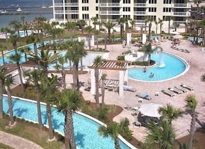 A resort pool area with multiple pools, palm trees, and lounge chairs. - Read my reviews.  Know what you are getting. (Fort Walton Beach)