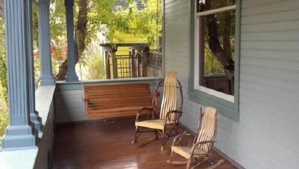 Une véranda avec un banc en bois et deux fauteuils à bascule.