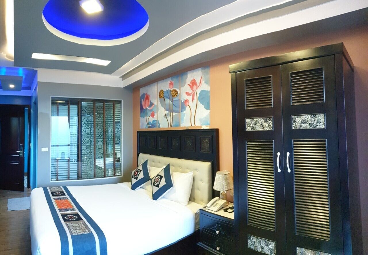 Quarto de hotel com uma cama grande, mesa de cabeceira, guarda-roupa e uma parede decorativa com arte floral.