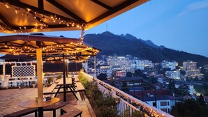 An outdoor seating area with tables and chairs, overlooking a cityscape with buildings and a mountain in the background. - Sapa Nature View Hotel (Sa Pa)