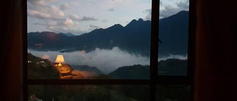 Vista desde una ventana sobre un paisaje montañoso, con una lámpara sobre una mesa.