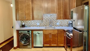 Una cocina moderna con armarios de madera, un refrigerador de acero inoxidable, un lavavajillas y una lavadora.