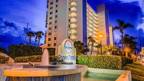 A hotel entrance with a sign, a fountain, and a pool area.