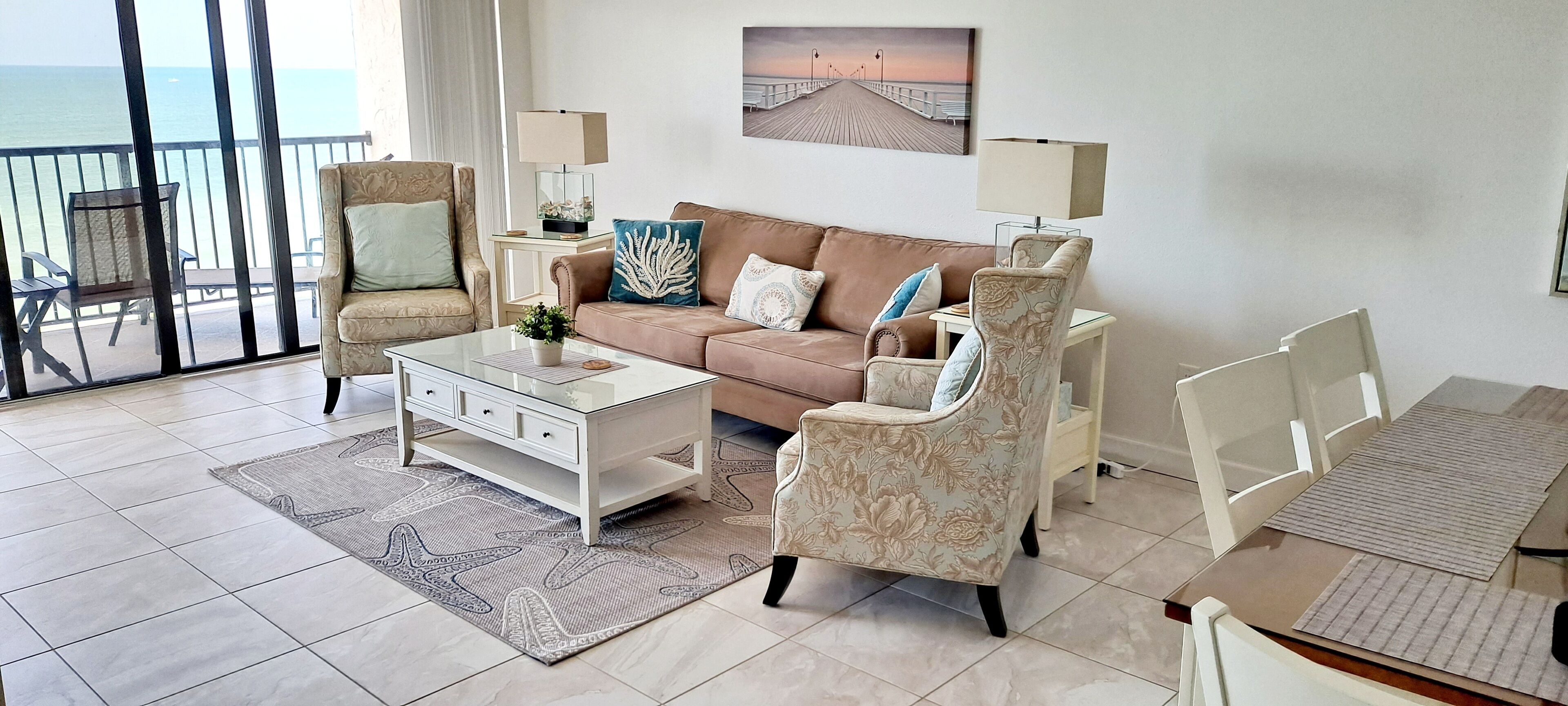Un salon comprenant un canapé, des fauteuils, une table basse et offrant une vue sur l’océan grâce à de grandes fenêtres.