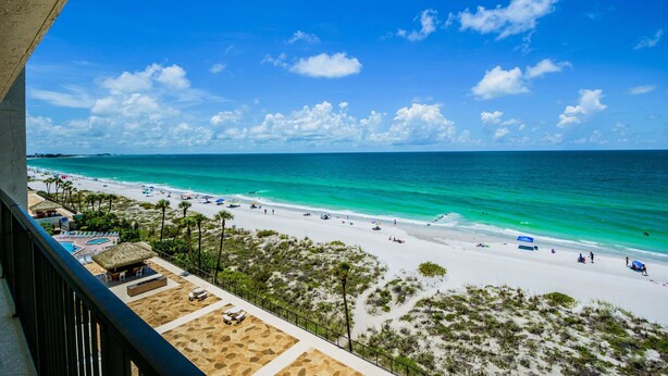 A beach view from a balcony with a pool area and beach umbrellas.