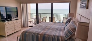 Camera d'albergo con un letto, una TV, una cassettiera, un balcone vista mare e un piccolo tavolo con sedie.