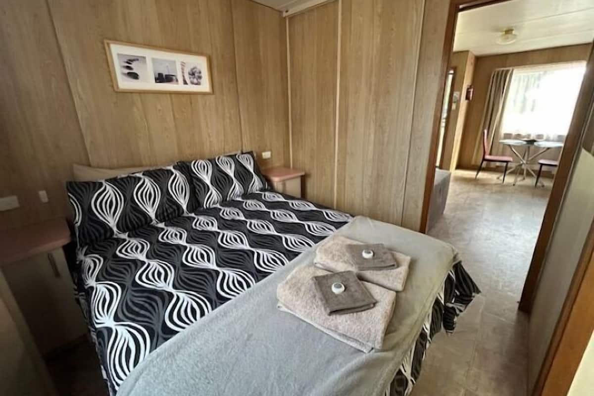 Een hotelkamer met een bed, een klein nachtkastje, een handdoekhouder en uitzicht op de ontbijtruimte.
