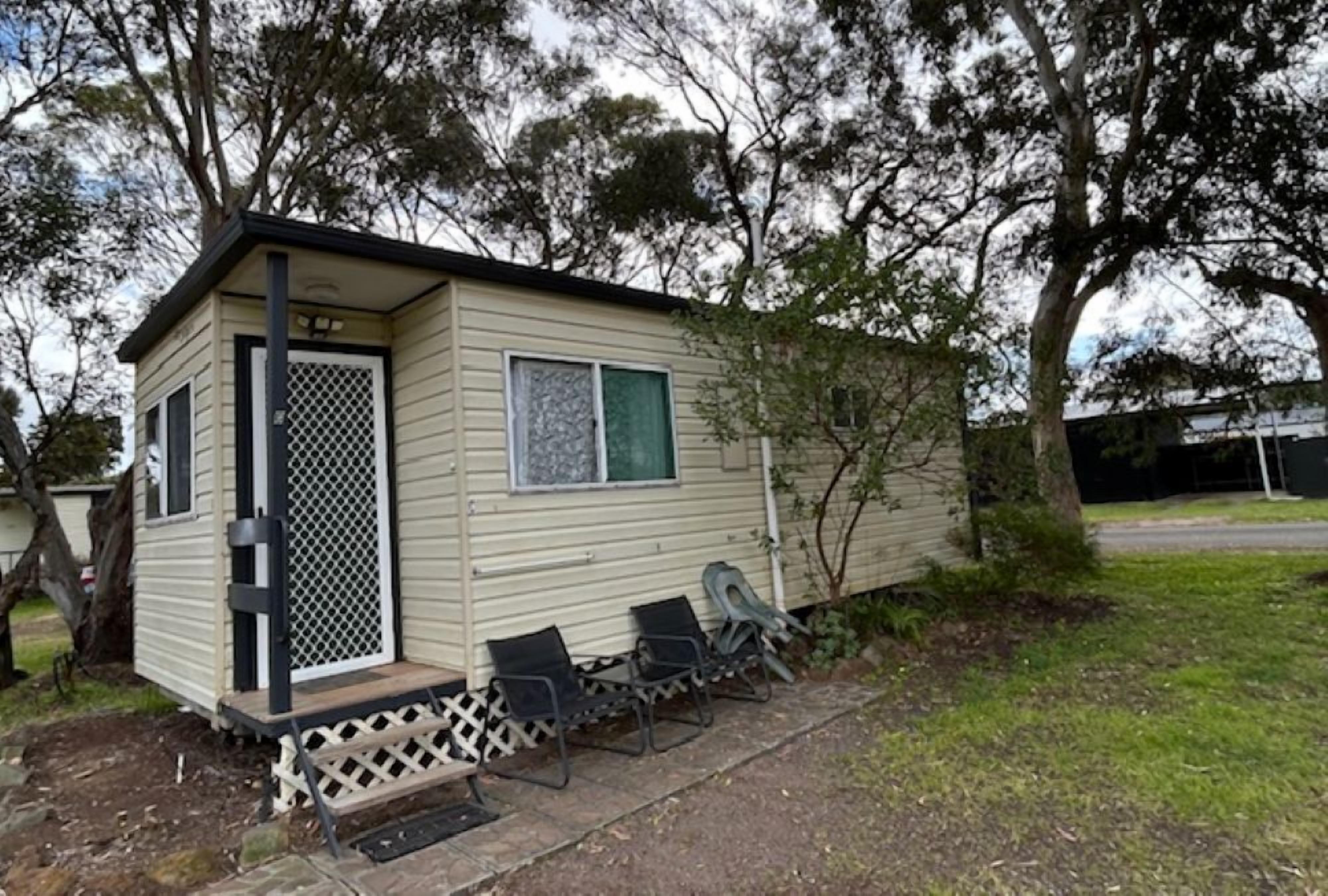 A small, single-story mobile home with a porch and three chairs.
