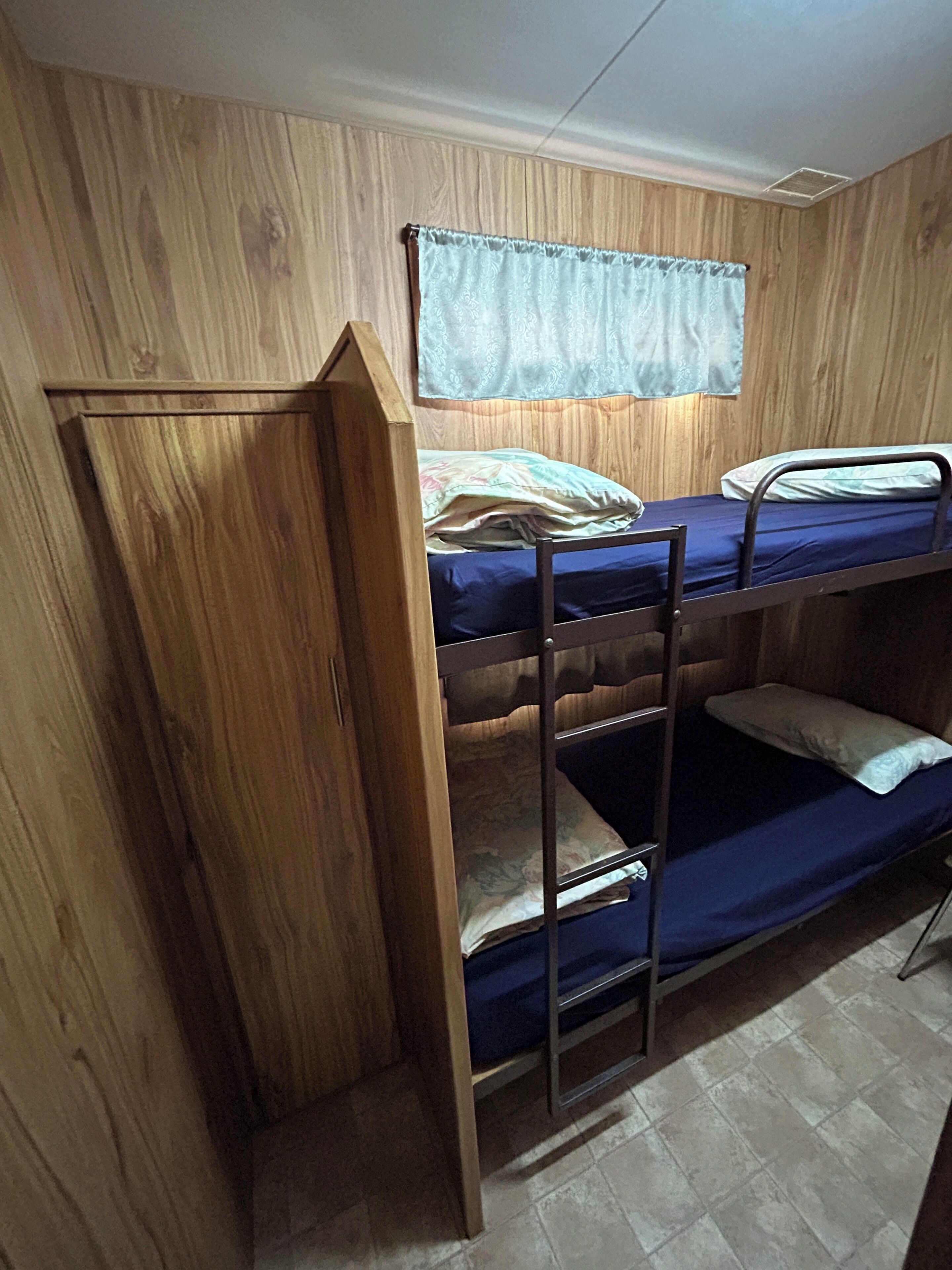A bunk bed room with wooden walls, a window with a curtain, and a tiled floor.
