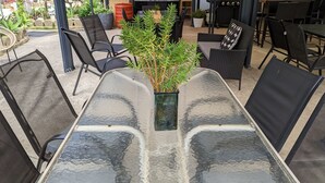 An outdoor patio area with a glass-top table, black mesh chairs, and a potted plant. - KI Caravan Park, Kingscote (Brownlow Ki)
