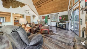Een ruime woonkamer met een hoog houten plafond, lederen meubels en een rustieke inrichting, waaronder een vachttapijt en geweihoren.