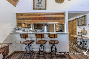 Un coin bar avec trois tabourets, un plafond en bois et une enseigne au-dessus du bar.