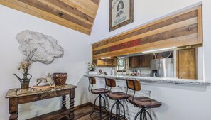 Une cuisine rustique avec des tabourets de bar en bois, une sculpture en pierre et un plafond en bois.