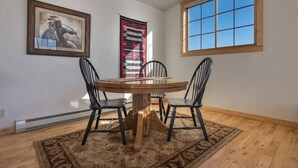 A dining area with a round table, four chairs, a patterned rug, a large window, and two framed artworks on the walls. - Unique Driggs Quiet Apartment (Driggs)