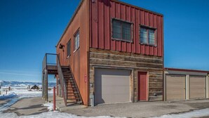 A red metal building with a garage and a staircase leading to a platform. - Unique Driggs Quiet Apartment (Driggs)