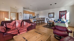A living room with a red leather sofa, a wooden coffee table, and a dining area with a wooden table and chairs. - Unique Driggs Quiet Apartment (Driggs)