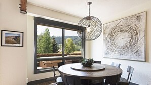 Un comedor con una mesa redonda, sillas, una lámpara colgante, un ventanal con vistas y una obra de arte enmarcada en la pared.