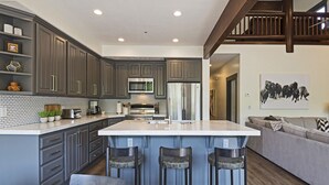 Una cocina moderna con armarios grises, una isla grande con taburetes de bar, un refrigerador de acero inoxidable y un microondas.