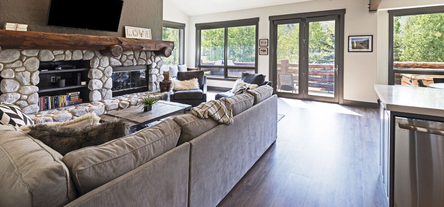 Ein geräumiges Wohnzimmer mit Kamin aus Stein, einem großen Sofa und einem flachbildfernseher an der Wand.