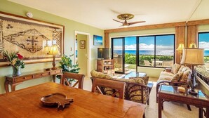 Un vaste salon doté d’une grande fenêtre donnant sur l’océan, un coin repas avec une table en bois et des sièges confortables.
