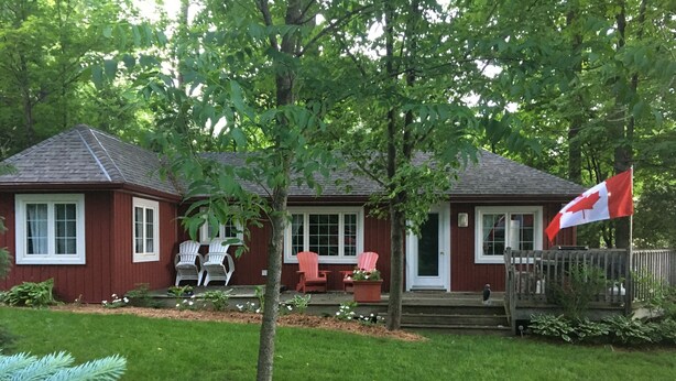 A red house with a porch, two white chairs, and a Canadian flag.
