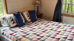 A bedroom with a large bed, a nightstand, a lamp, and a window with curtains.
