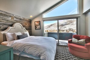 Ein Schlafzimmer mit einem großen Bett, einem roten Sessel und Blick auf eine verschneite Landschaft durch ein großes Fenster.