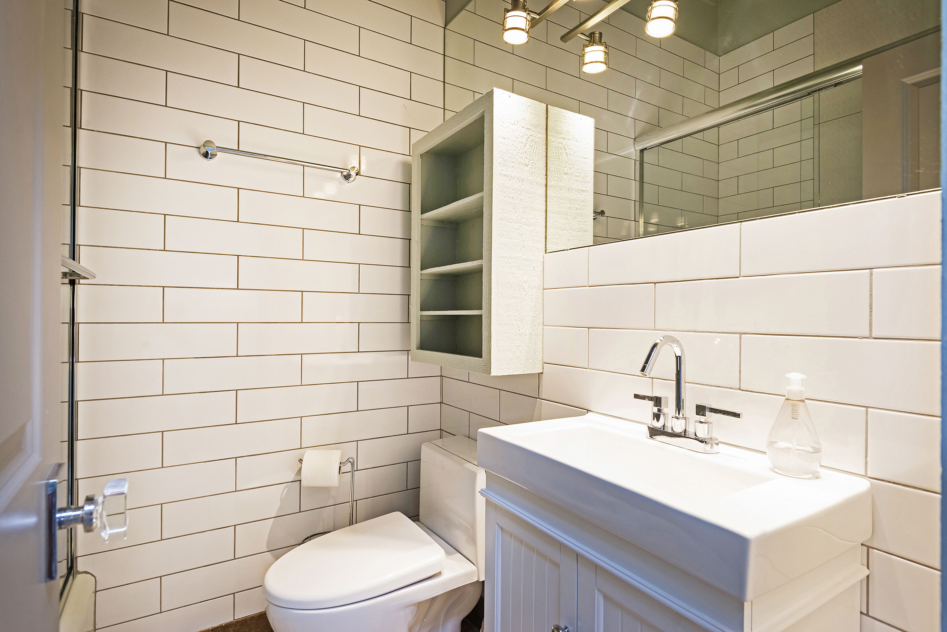A bathroom with white subway tiles, a white toilet, a white sink with a mirror above it, and a towel rack.